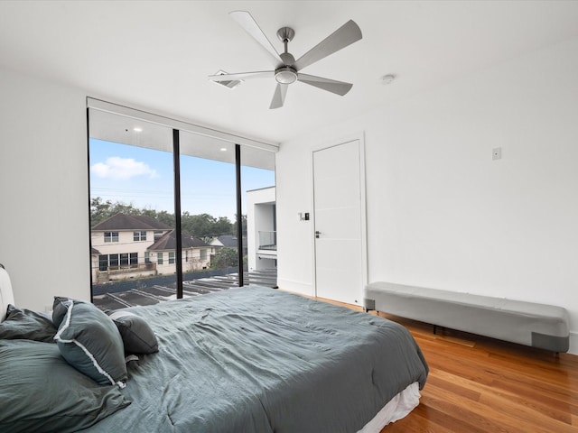 bedroom featuring access to exterior, a ceiling fan, a wall of windows, and wood finished floors