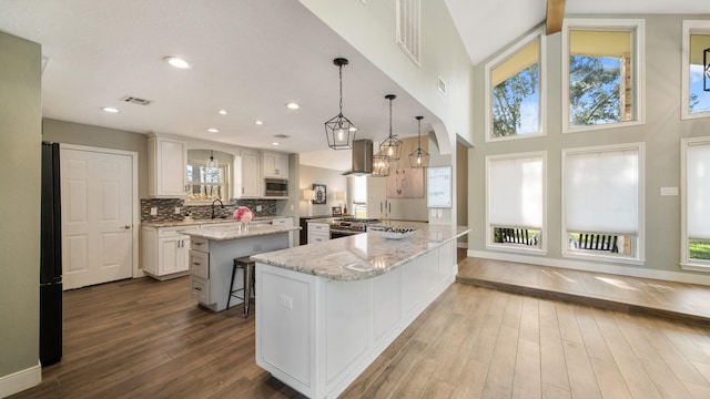 kitchen featuring a kitchen bar, white cabinetry, decorative light fixtures, stainless steel appliances, and light stone countertops