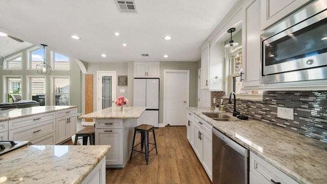 kitchen with hanging light fixtures, stainless steel appliances, white cabinets, and a kitchen bar