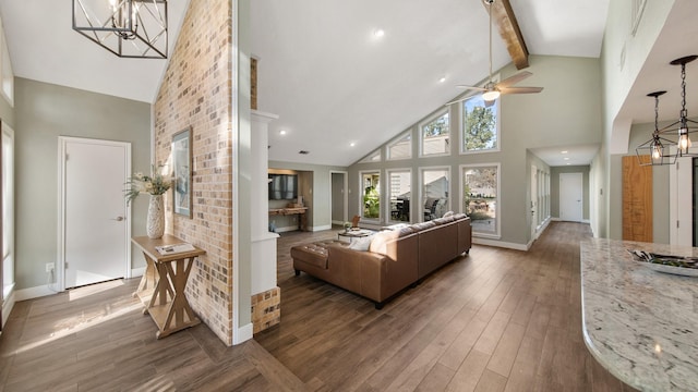 living room with beam ceiling, dark wood-type flooring, ceiling fan with notable chandelier, and high vaulted ceiling