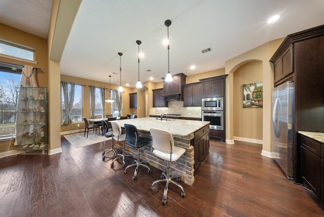 kitchen featuring pendant lighting, sink, a kitchen island with sink, stainless steel appliances, and light stone counters