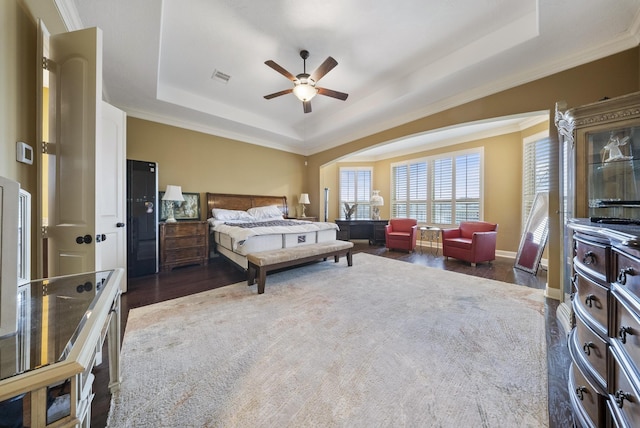 bedroom featuring dark wood-type flooring, ceiling fan, ornamental molding, and a tray ceiling