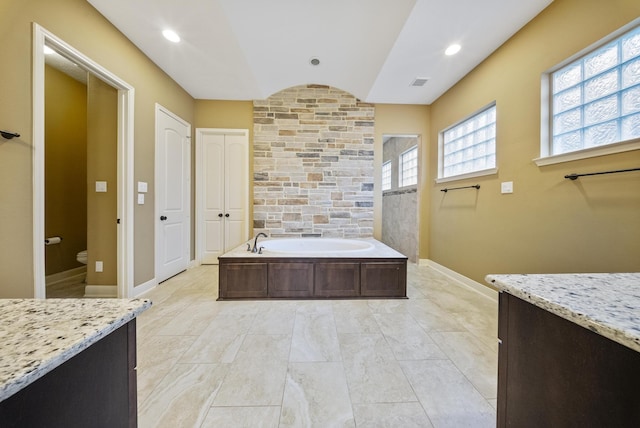 bathroom featuring vanity, toilet, vaulted ceiling, and a tub