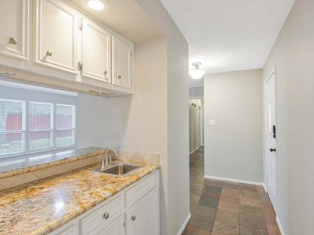 kitchen with light stone counters, sink, and white cabinets