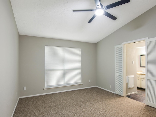 unfurnished bedroom featuring lofted ceiling, dark carpet, connected bathroom, and ceiling fan