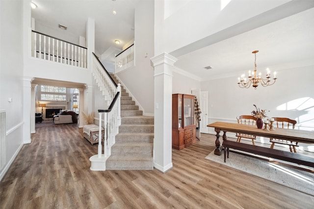 foyer featuring ornate columns, crown molding, wood-type flooring, a notable chandelier, and a high ceiling