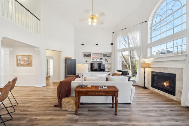 living room featuring ceiling fan, a towering ceiling, a fireplace, and wood-type flooring