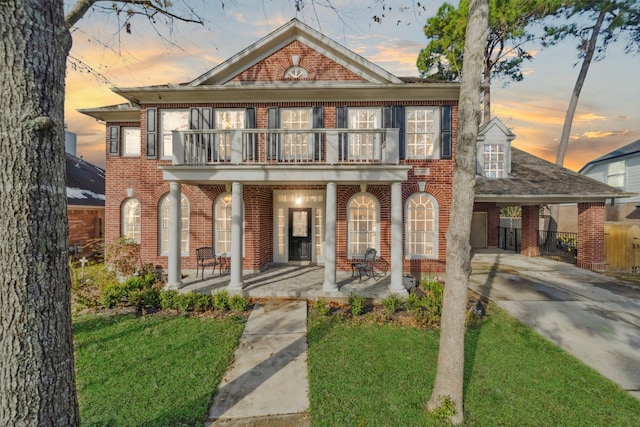 view of front facade featuring a carport, a balcony, a yard, and covered porch