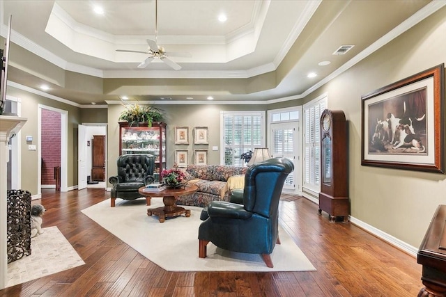 living room with ornamental molding, dark wood-type flooring, ceiling fan, and a tray ceiling