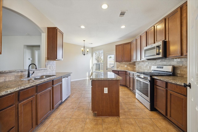 kitchen with a kitchen island, decorative light fixtures, sink, stainless steel appliances, and light stone countertops