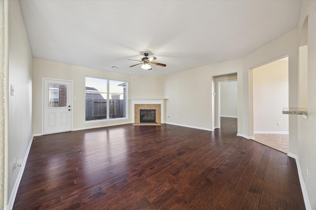 unfurnished living room with ceiling fan, dark hardwood / wood-style flooring, and a tile fireplace