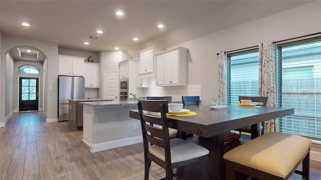 kitchen with white cabinetry, stainless steel appliances, light stone counters, tasteful backsplash, and light hardwood / wood-style floors