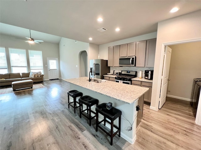 kitchen with appliances with stainless steel finishes, gray cabinetry, a kitchen breakfast bar, tasteful backsplash, and a center island with sink