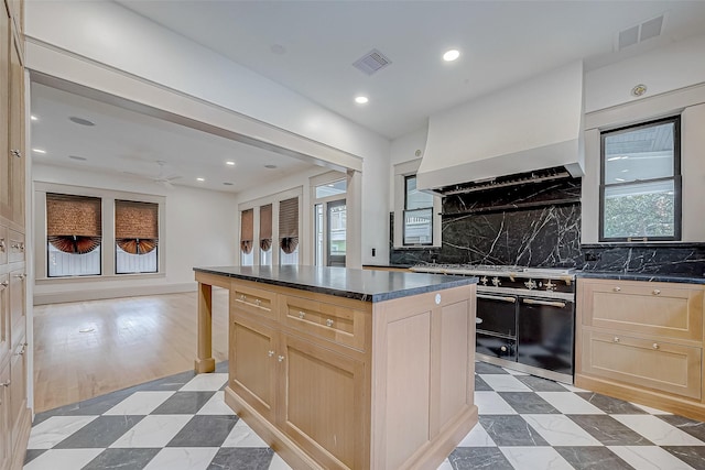 kitchen featuring premium range hood, backsplash, a center island, light brown cabinetry, and range with two ovens