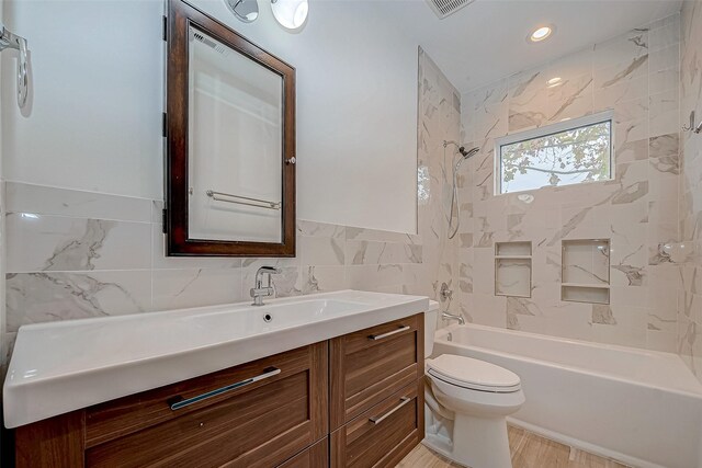 full bathroom with tile walls, vanity, tiled shower / bath combo, and toilet