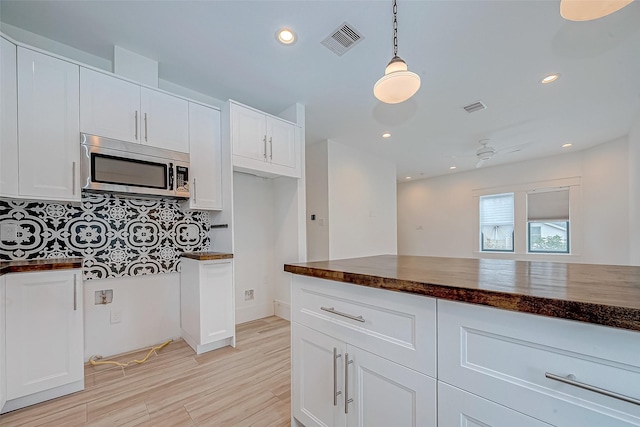 kitchen with tasteful backsplash, white cabinetry, pendant lighting, and light wood-type flooring