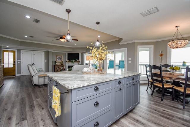 kitchen with dark wood-type flooring, gray cabinetry, ornamental molding, a kitchen island, and pendant lighting