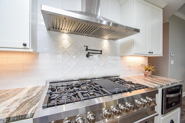 kitchen with wall chimney range hood, appliances with stainless steel finishes, light stone counters, white cabinets, and decorative backsplash