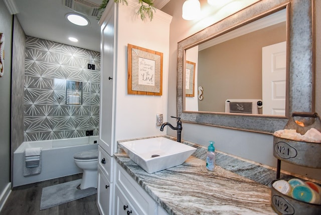 full bathroom featuring hardwood / wood-style flooring, vanity, ornamental molding, toilet, and bathing tub / shower combination