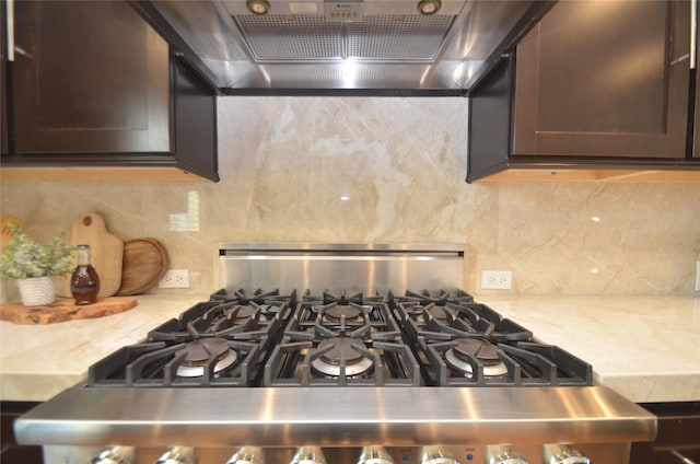 room details with dark brown cabinetry, range hood, stainless steel range with gas cooktop, and tasteful backsplash