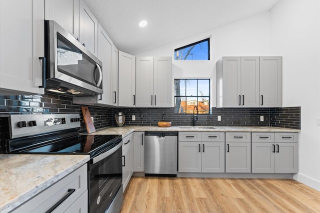 kitchen featuring appliances with stainless steel finishes, lofted ceiling, sink, light hardwood / wood-style floors, and light stone countertops