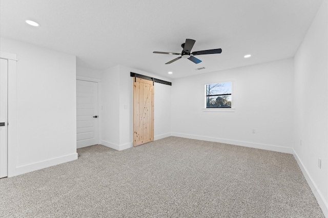 unfurnished bedroom featuring ceiling fan, a barn door, and carpet