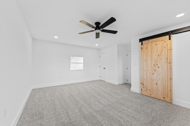 unfurnished bedroom with a barn door, ceiling fan, and carpet