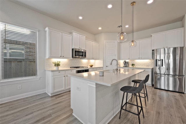 kitchen with sink, appliances with stainless steel finishes, hanging light fixtures, an island with sink, and white cabinets