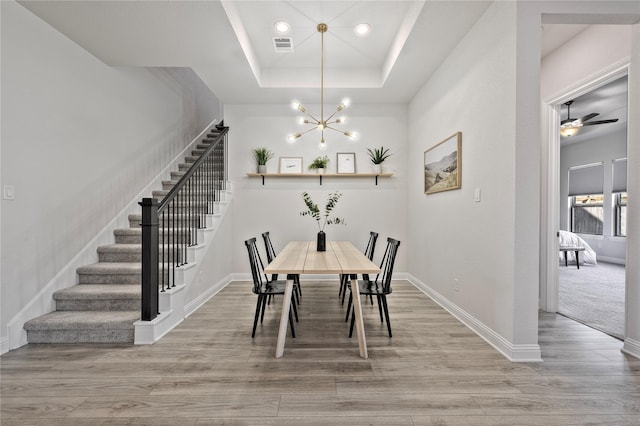 dining area with a raised ceiling, an inviting chandelier, and light hardwood / wood-style flooring