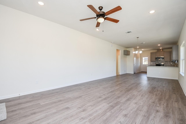 unfurnished living room with ceiling fan with notable chandelier and light hardwood / wood-style flooring