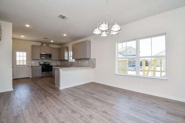 kitchen featuring hardwood / wood-style floors, decorative backsplash, kitchen peninsula, stainless steel appliances, and a healthy amount of sunlight