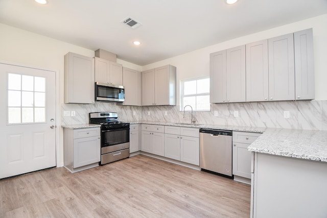 kitchen with sink, light hardwood / wood-style flooring, stainless steel appliances, light stone counters, and tasteful backsplash