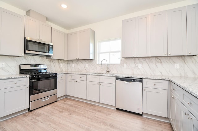 kitchen featuring sink, appliances with stainless steel finishes, light stone countertops, light hardwood / wood-style floors, and decorative backsplash