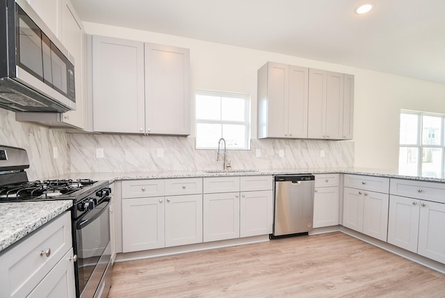 kitchen featuring sink, light stone counters, light wood-type flooring, appliances with stainless steel finishes, and backsplash