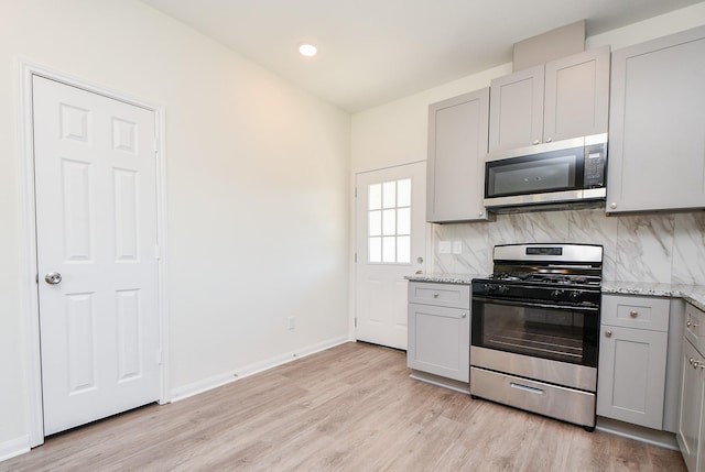 kitchen featuring gray cabinets, appliances with stainless steel finishes, decorative backsplash, light stone countertops, and light hardwood / wood-style flooring