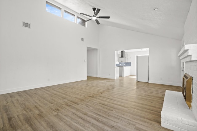 unfurnished living room featuring ceiling fan, a towering ceiling, a fireplace, and light hardwood / wood-style flooring