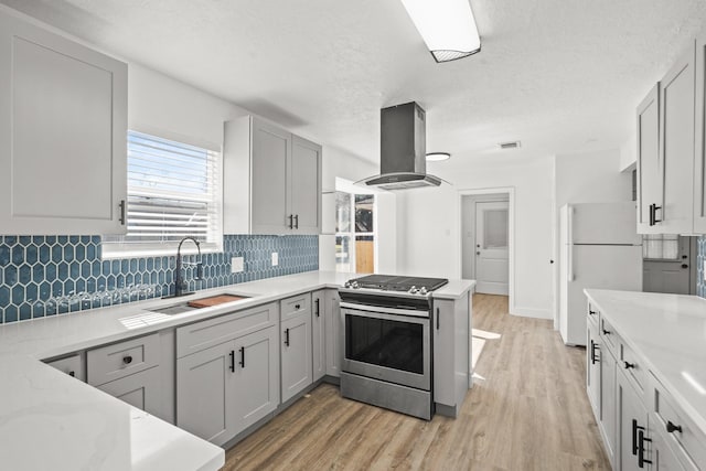 kitchen with sink, gray cabinets, island range hood, gas range, and white fridge