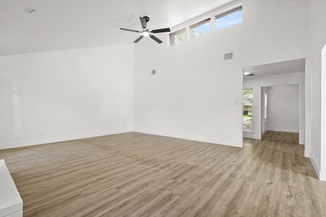 unfurnished living room with a high ceiling, ceiling fan, plenty of natural light, and light hardwood / wood-style floors