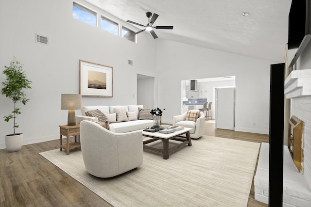 living room with wood-type flooring, high vaulted ceiling, ceiling fan, and a fireplace