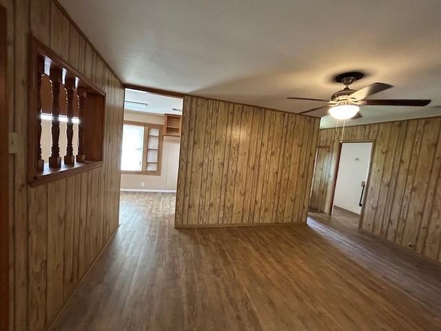 empty room with hardwood / wood-style floors, ceiling fan, and wood walls