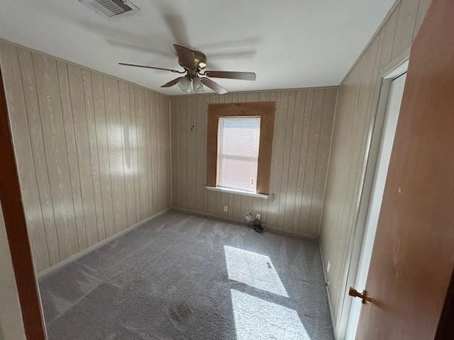 carpeted spare room with ceiling fan and wood walls