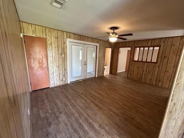 unfurnished bedroom with french doors, ceiling fan, wooden walls, and dark wood-type flooring