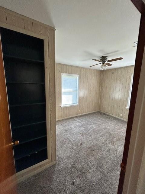 carpeted spare room with ceiling fan and wood walls