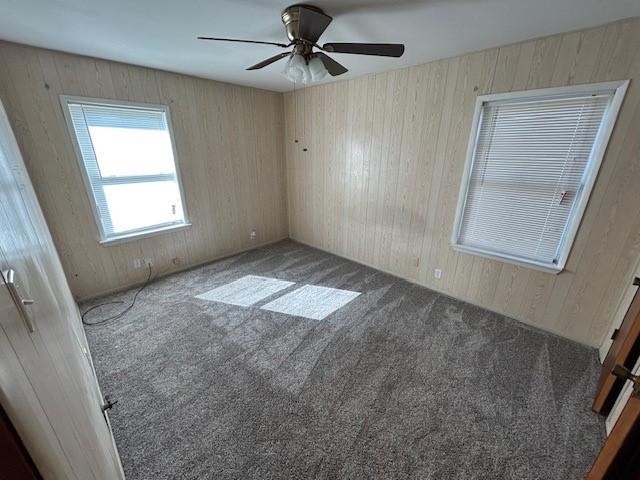 spare room with ceiling fan, dark carpet, and wooden walls