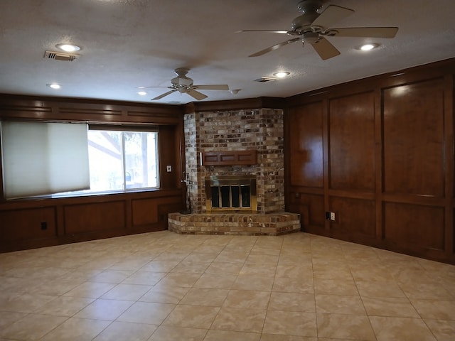 unfurnished living room featuring ceiling fan, a fireplace, a textured ceiling, and wood walls