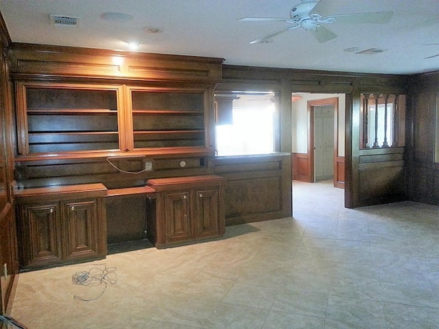 unfurnished office featuring built in desk, wooden walls, and ceiling fan