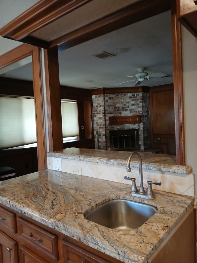 kitchen with light stone counters, ceiling fan, sink, and a brick fireplace