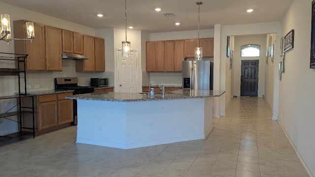 kitchen featuring sink, dark stone countertops, stainless steel appliances, an island with sink, and decorative backsplash