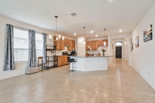 kitchen featuring pendant lighting, stainless steel range oven, an island with sink, and dark stone countertops