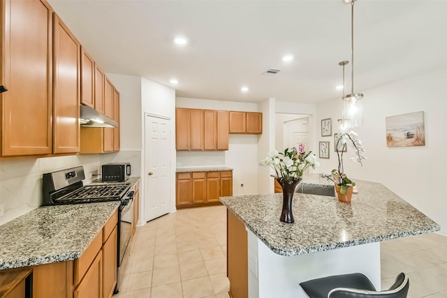 kitchen featuring pendant lighting, stainless steel range with gas stovetop, light stone countertops, and a center island with sink